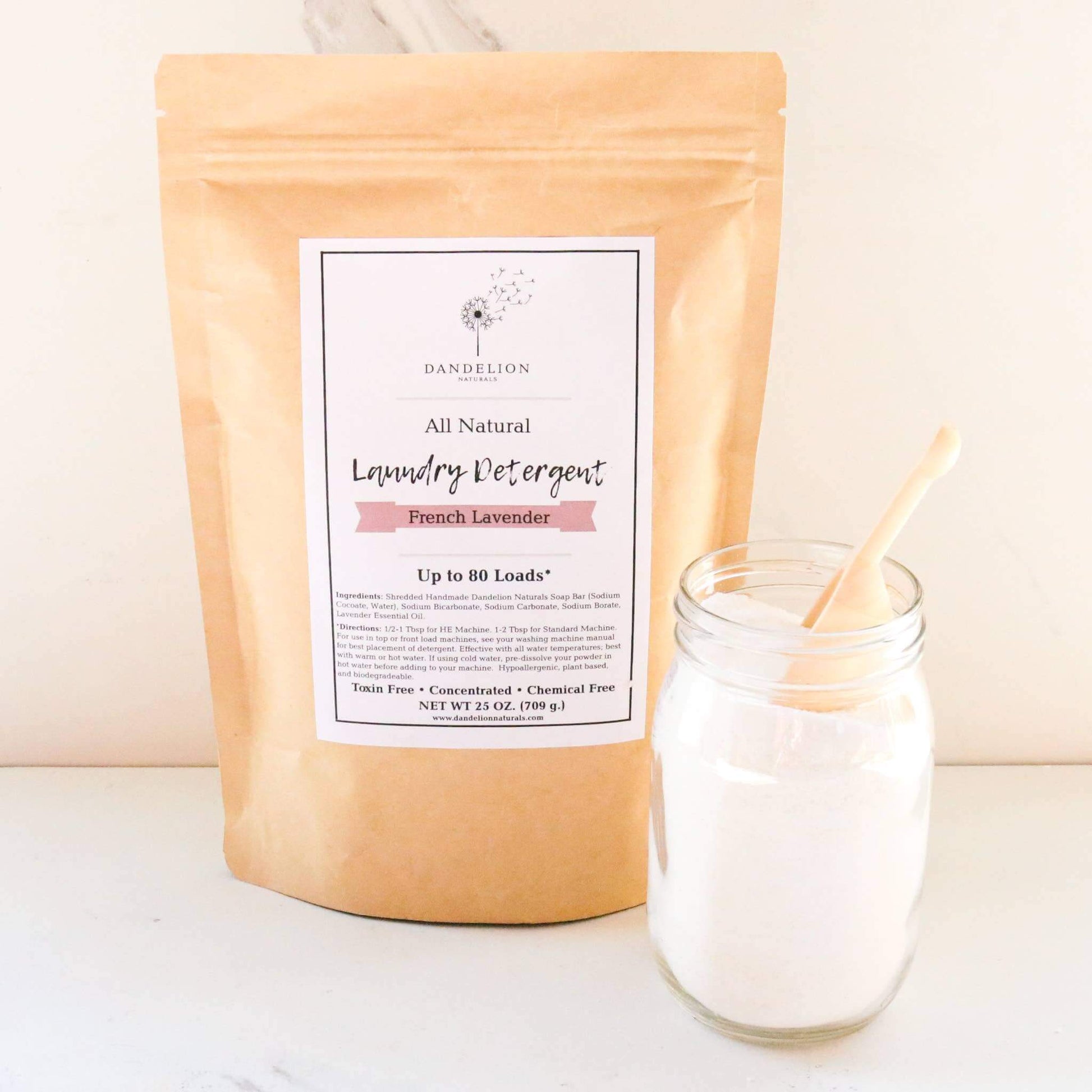 Non toxic laundry detergent in lavender scent in a resealable brown bag with a clear glass jar filled with laundry powder and a wood spoon.