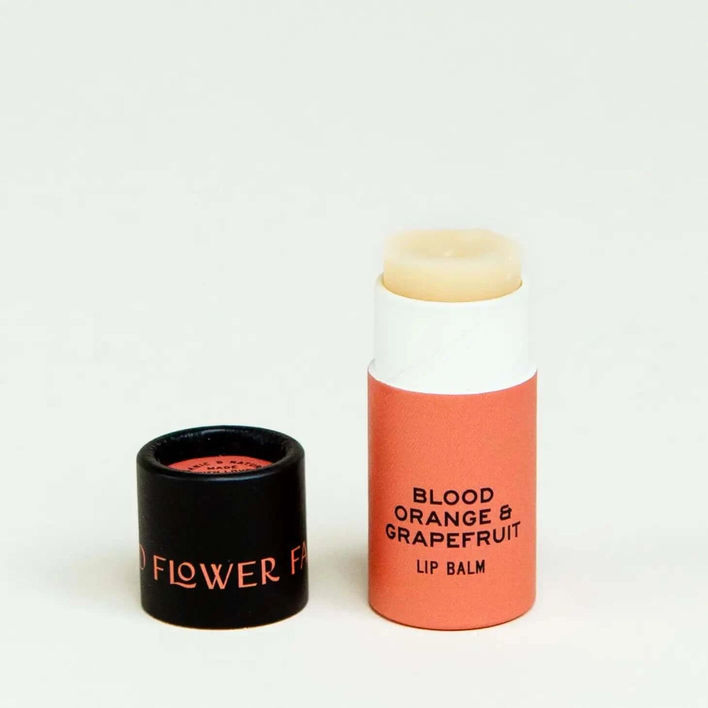 blood orange and grapefruit organic lip balm in a biodegradable container with the lid off and placed next to it