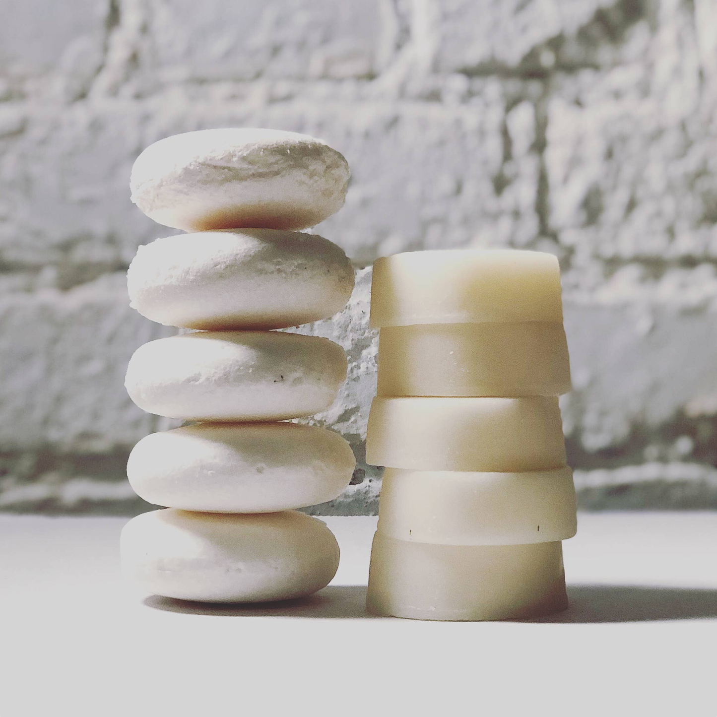 Five shampoo bars stacked on top of each other, sitting next to five conditioner bars stacked on top of each other.