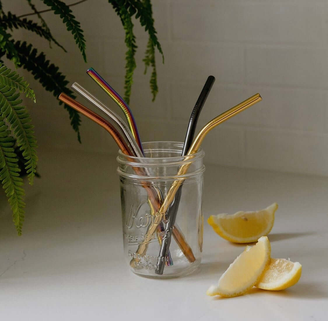 An empty clear glass with several different color stainless steel straws in it.