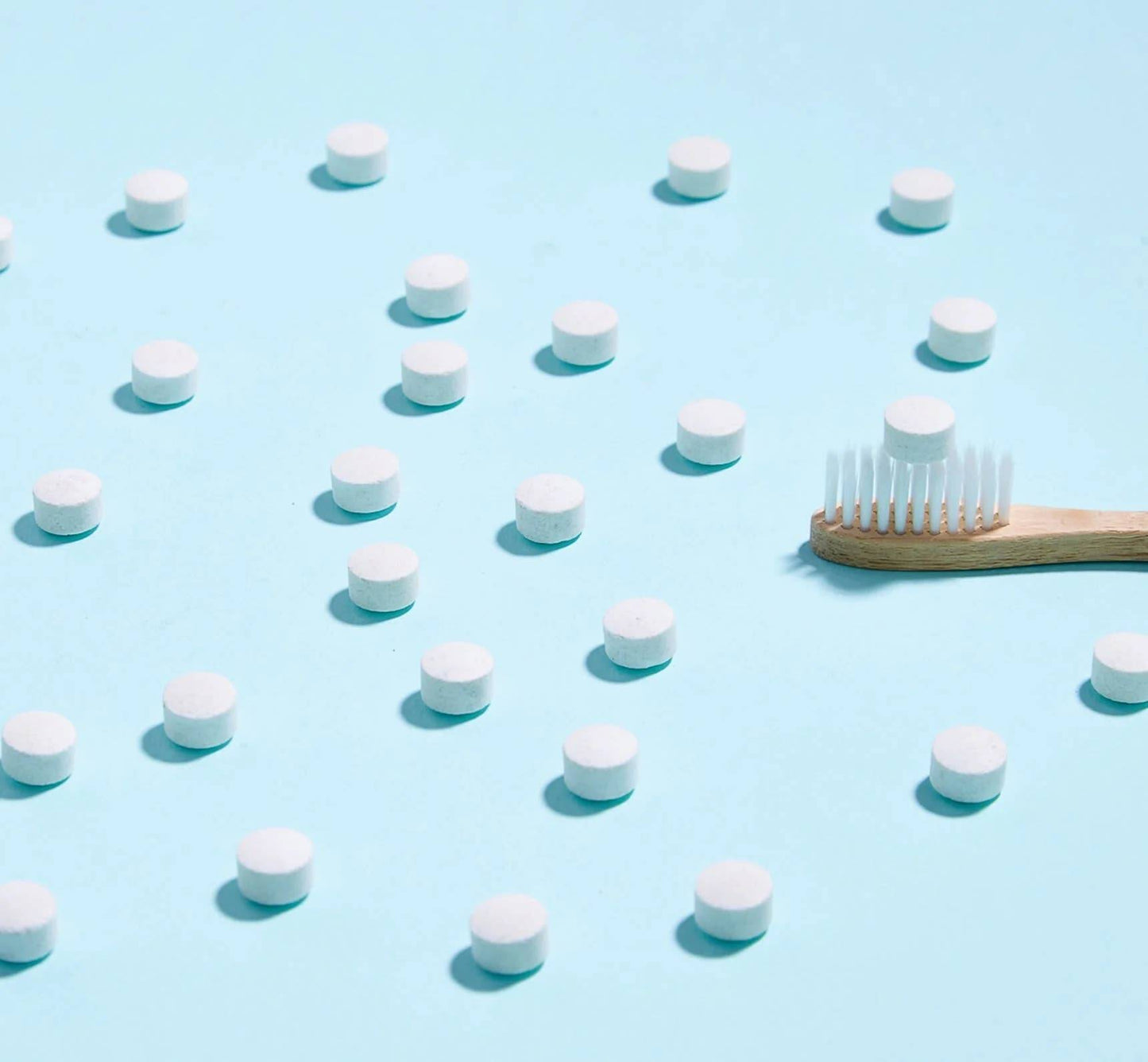 White toothpaste tablets and a bamboo toothbrush with a tablet on it.